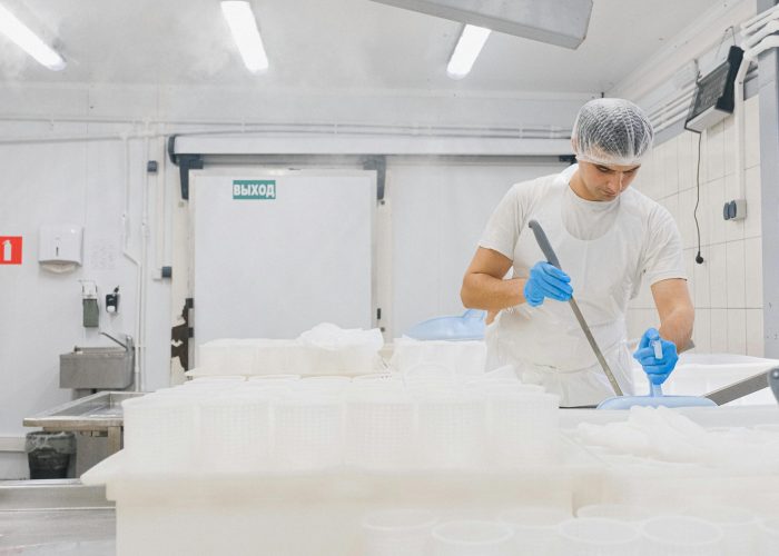 Man in sterile gear working in a cheese production facility, ensuring hygiene standards.
